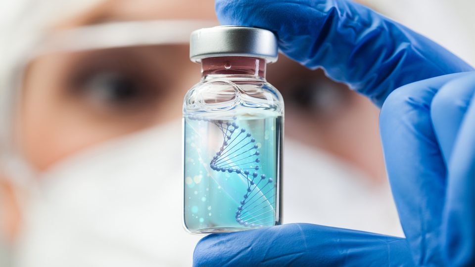 A researcher holds up a vial of liquid containing a strand of DNA.