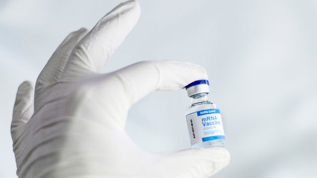 Gloved hand holding a vial of SARS-CoV-2 mRNA vaccine. 