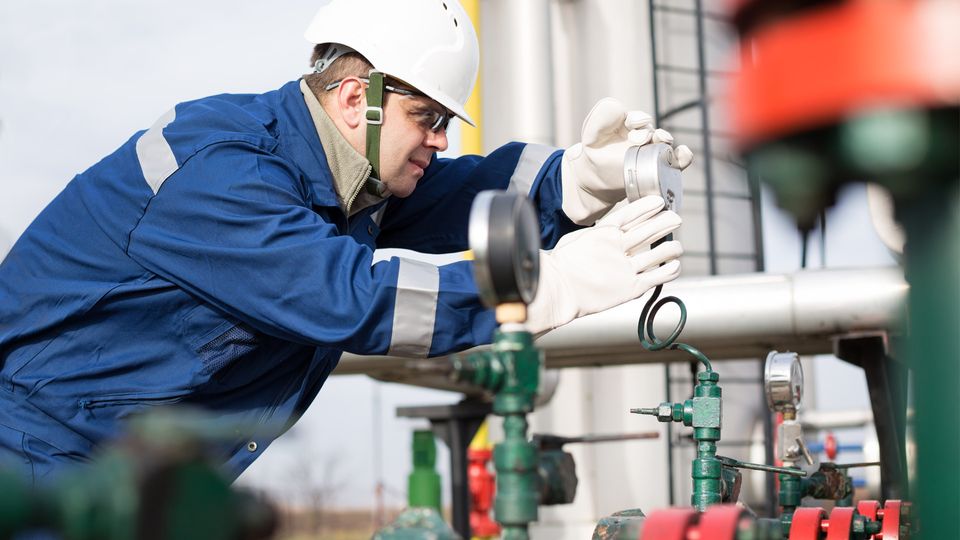 A worker looks at a pressure gauge on green pipes. 