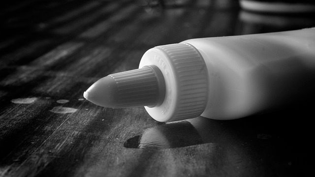 Black and white shot of a container of craft glue on its side on a table. 