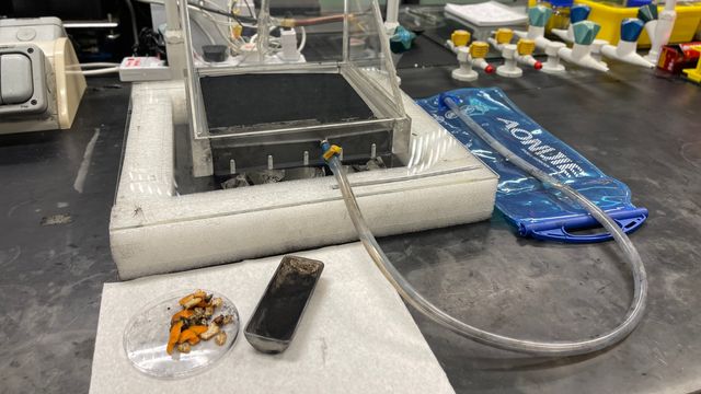 A prototype of the solar still, some orange peel in a dish and a container of MXene powder with a lab in the background. 