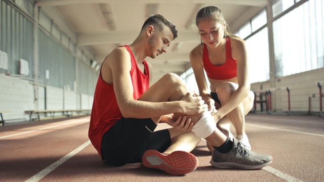 A woman wraps a man's leg with a bandage. 