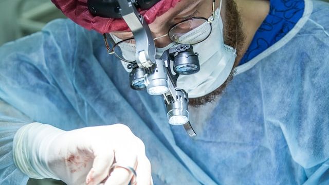 A surgeon operating on a patient using a head mounted optical tool for precision work. 