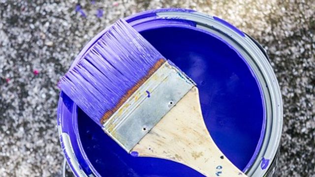 Paintbrush resting on top of an open tin of purple paint. 