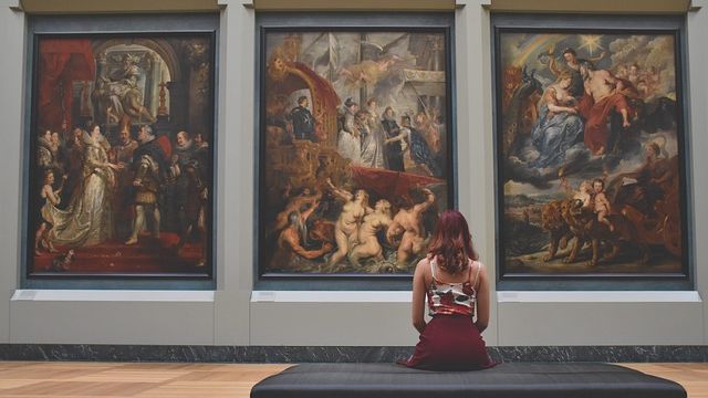 A woman sitting in an art gallery in front of three large paintings. 